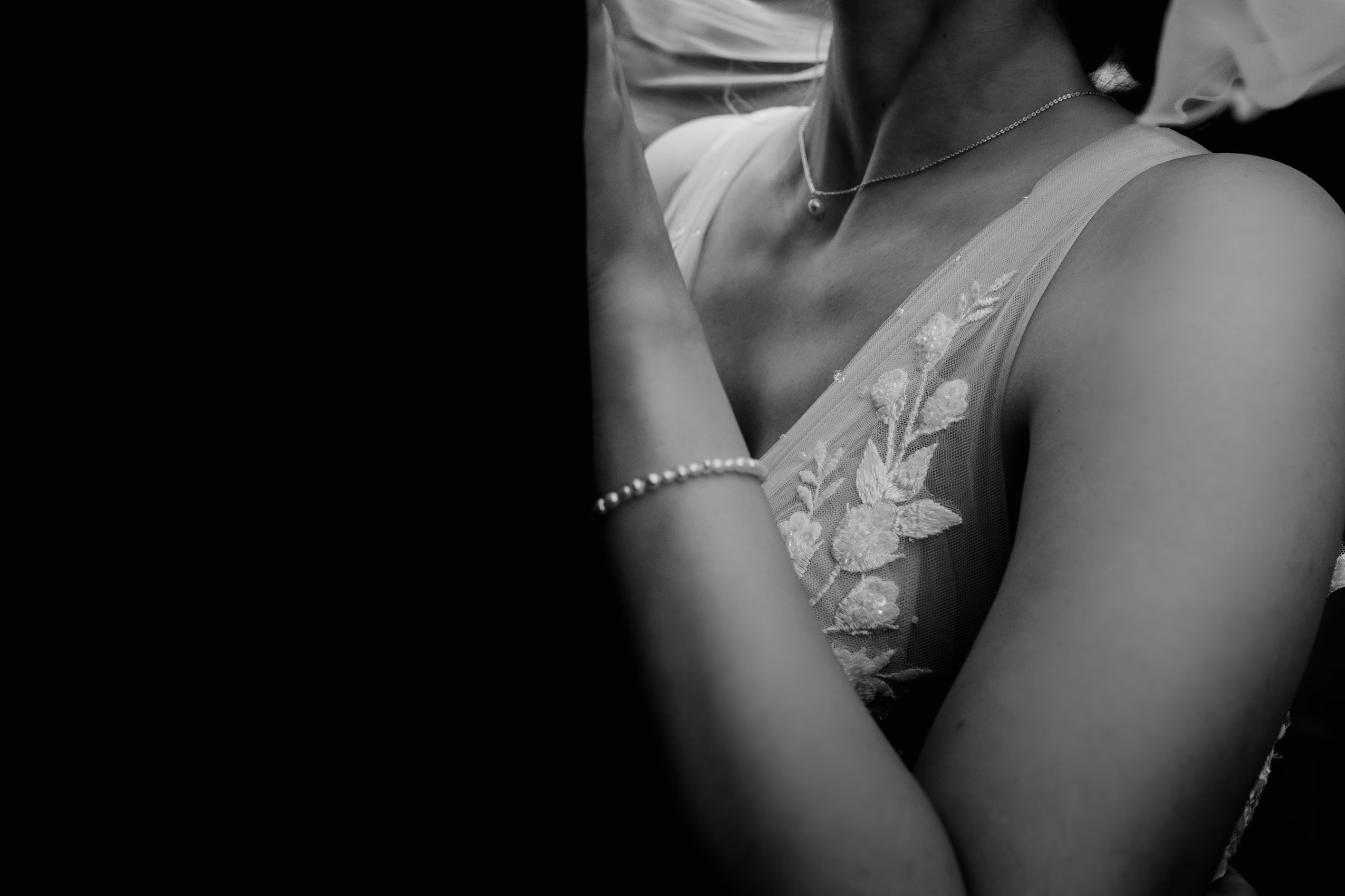 Hochzeitsfotografische Detailaufnahme des Hochzeitspaars. Man sieht das detailreiche Blumenmuster auf dem Brautkleider der Braut