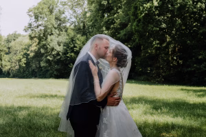 Intimer Moment des Brautpaars unter dem Schleier der Braut in Front eines grünen Waldes